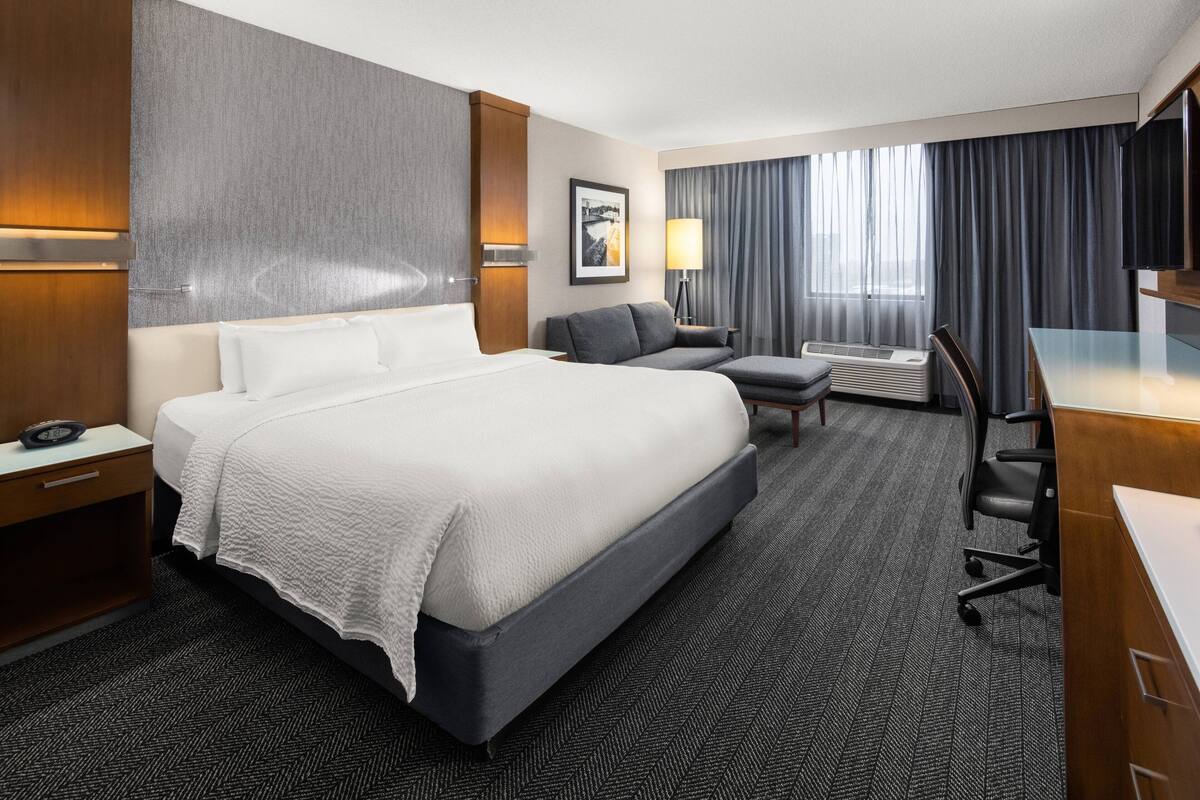 Een hotelkamer met een groot bed, een bureau, een stoel, een bank, een televisie en een raam met gordijnen.