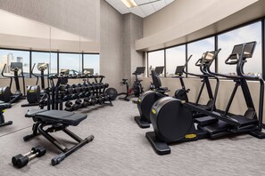 Une salle de sport moderne dotée de divers équipements d’exercice, de grandes fenêtres offrant une vue sur la ville et d’un espace intérieur vaste et bien aménagé.