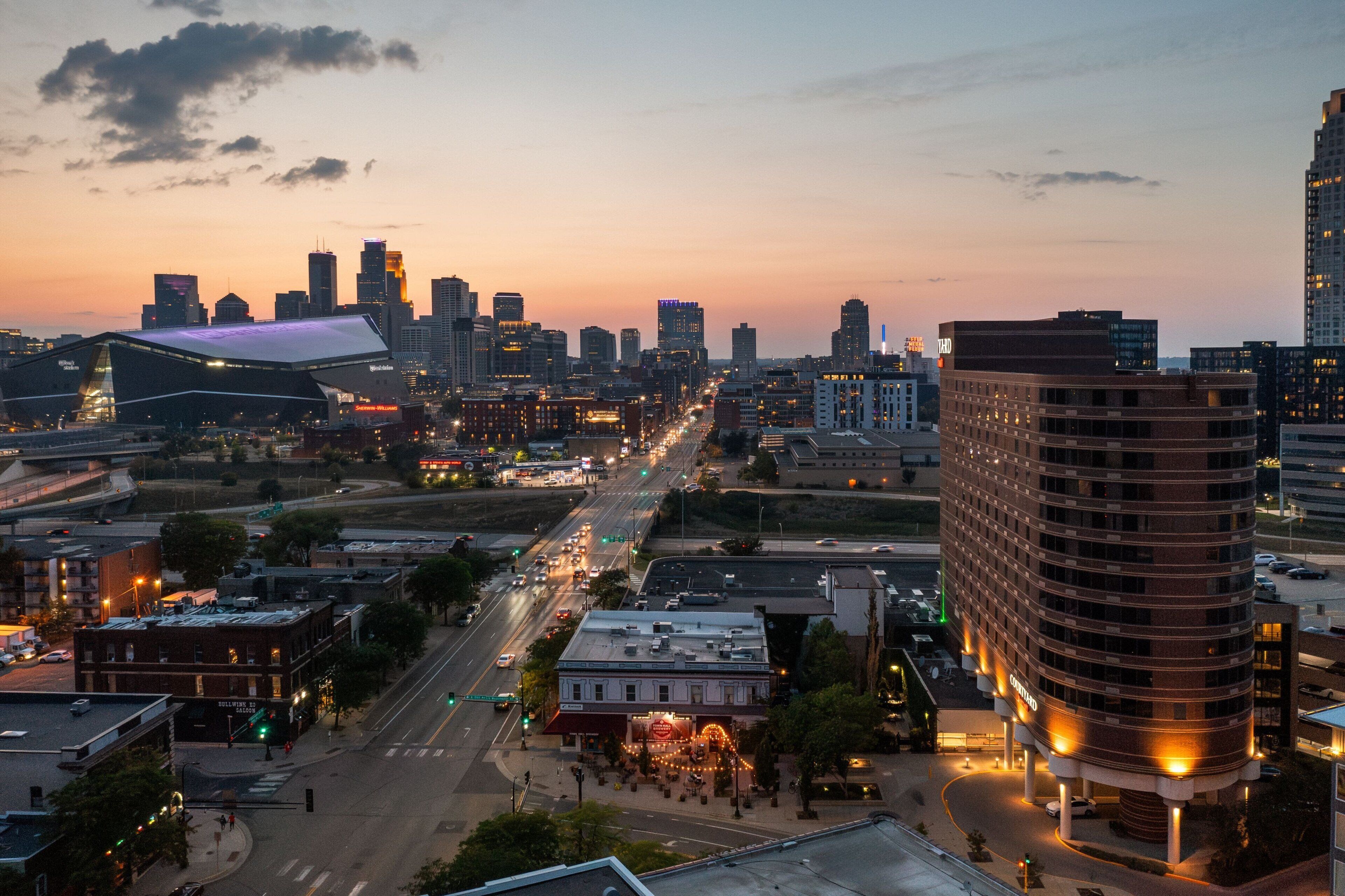 A cityscape with a prominent curved building on the right and a large, modern building with a flat roof on the left.