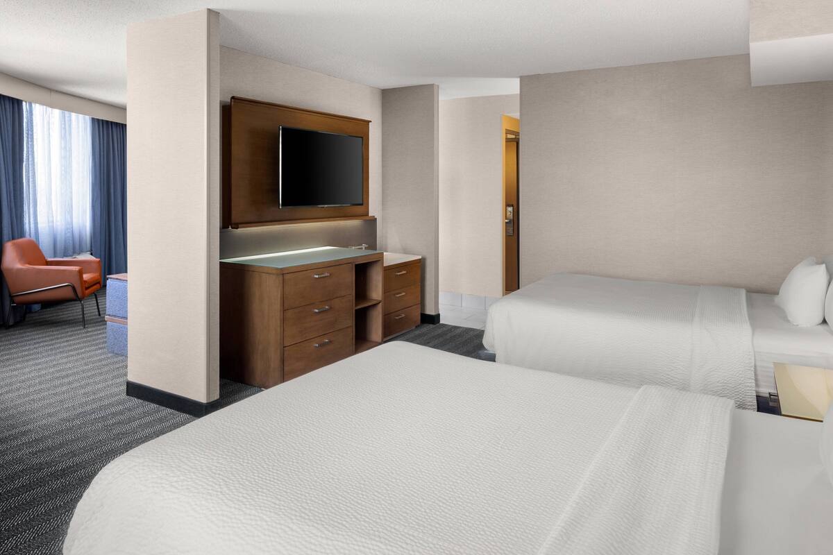 Hotelkamer met twee bedden, een bureau, een flatscreen televisie, een stoel en een groot raam met gordijnen.