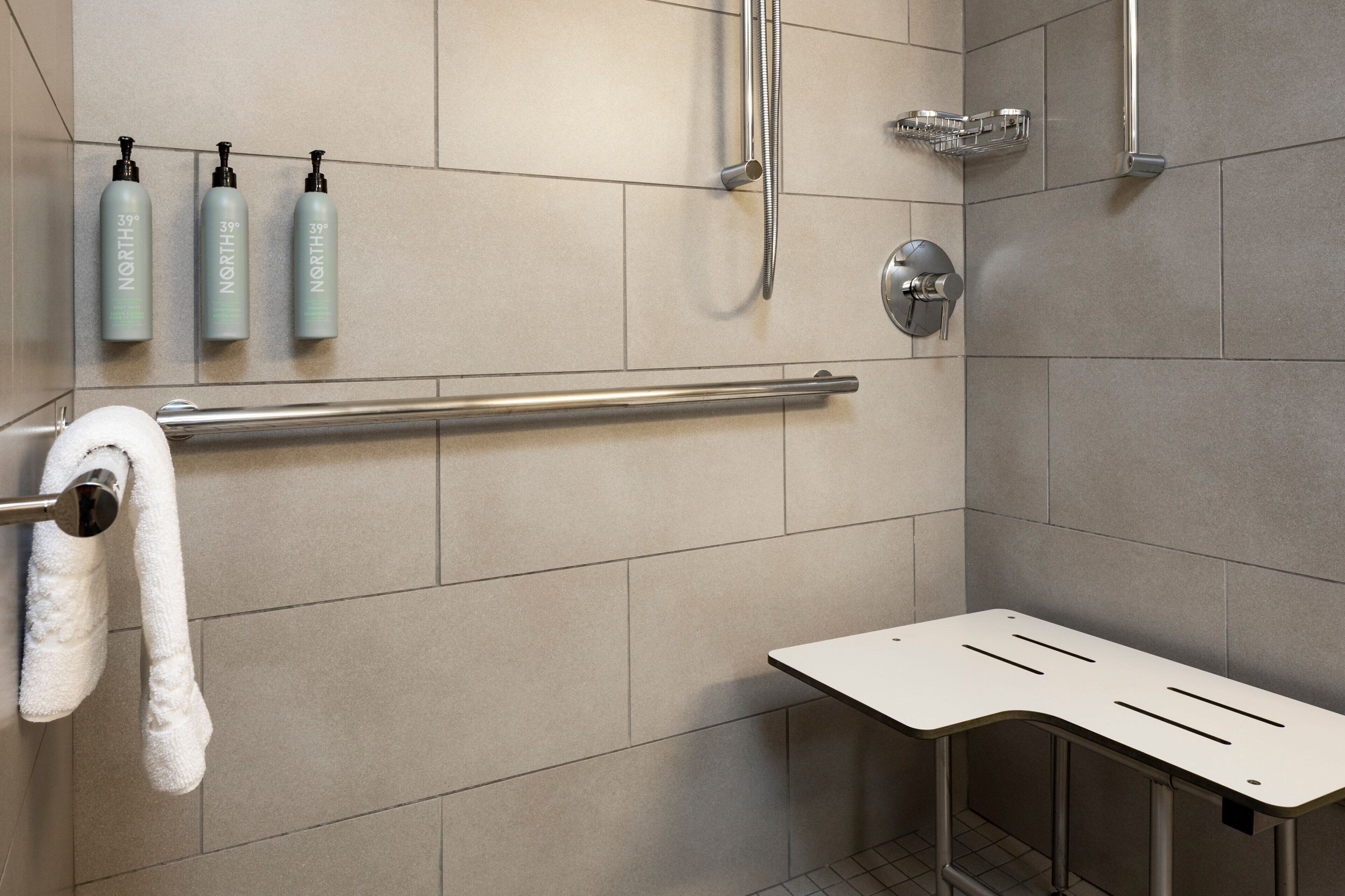 A modern shower area with a grab bar, three bottles of shampoo, and a towel rack.