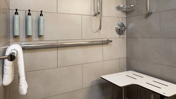 A modern shower area with a grab bar, three bottles of shampoo, and a towel rack.