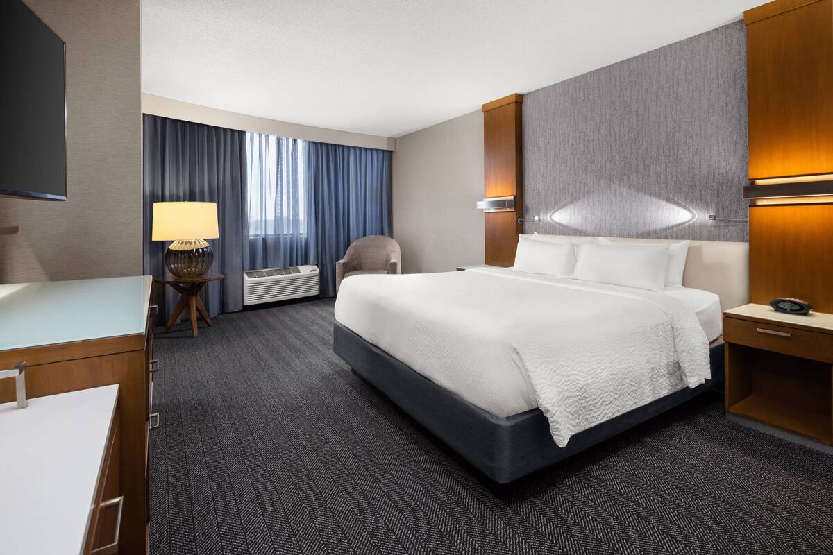 Hotelkamer met een groot bed, een bureau, een stoel, een lamp en een tv aan de muur.