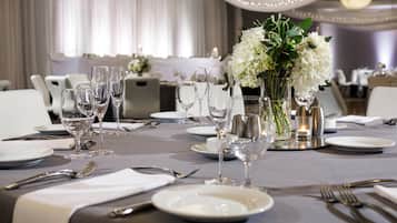 A dining table set with white plates, silverware, and clear glasses, with a centerpiece of white flowers and candles.