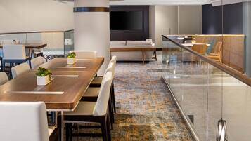 A modern conference room with a long table, comfortable seating, a large flat-screen TV, and a patterned carpet.