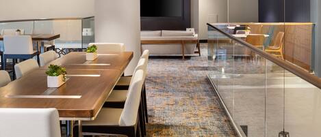 A modern conference room with a long table, comfortable seating, a large flat-screen TV, and a patterned carpet.