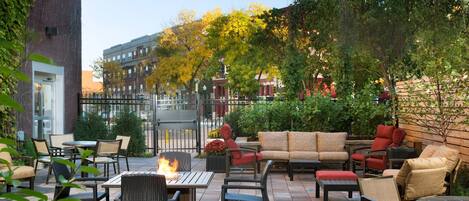 An outdoor patio with wicker furniture, a fire table, and a view of buildings in the background.