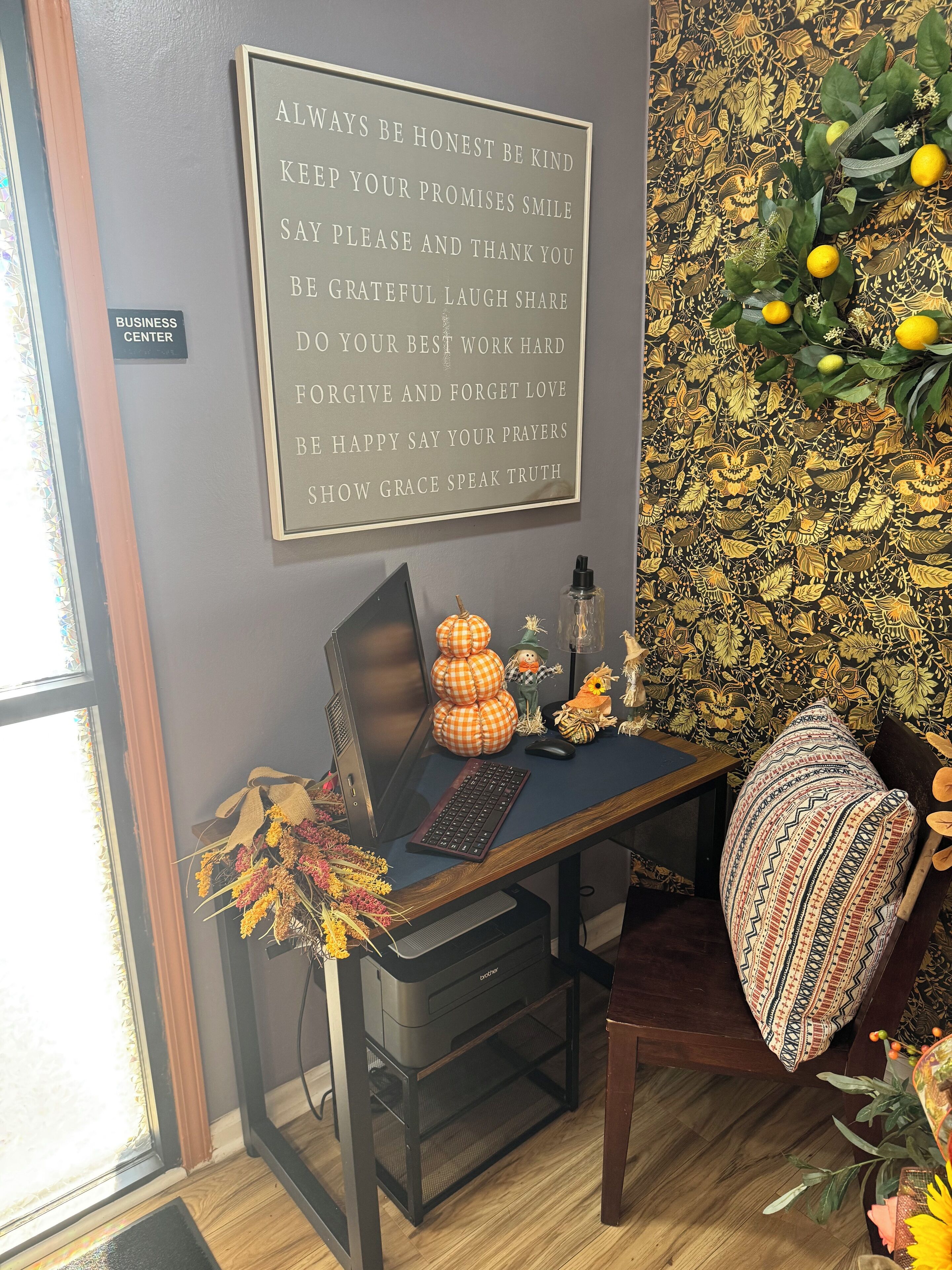 A workspace with a desk, computer, keyboard, and decorative items including a pumpkin and a scarecrow. A motivational quote is displayed on the wall.