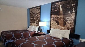 Habitación de hotel con dos camas, una mesita de noche con lámpara y un cuadro grande con una cascada en la pared.