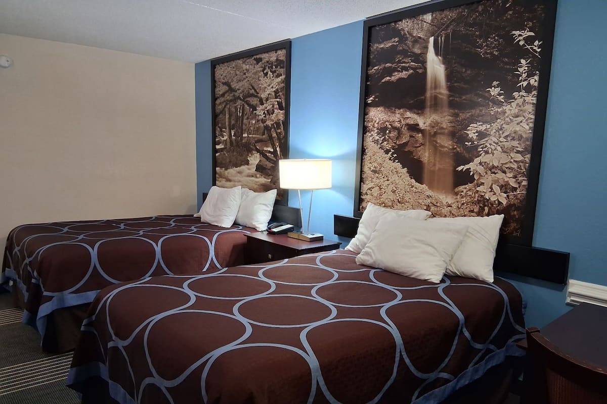 A hotel room with two beds, a nightstand with a lamp, and a large framed picture of a waterfall on the wall.