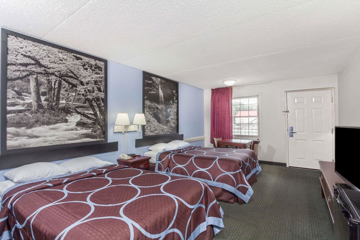 A hotel room with two beds, a TV, a desk, and large black-and-white landscape pictures on the wall.