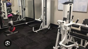 Un gimnasio con varias máquinas de ejercicio, un espejo grande y un ventanal con vistas a un tanque de agua.
