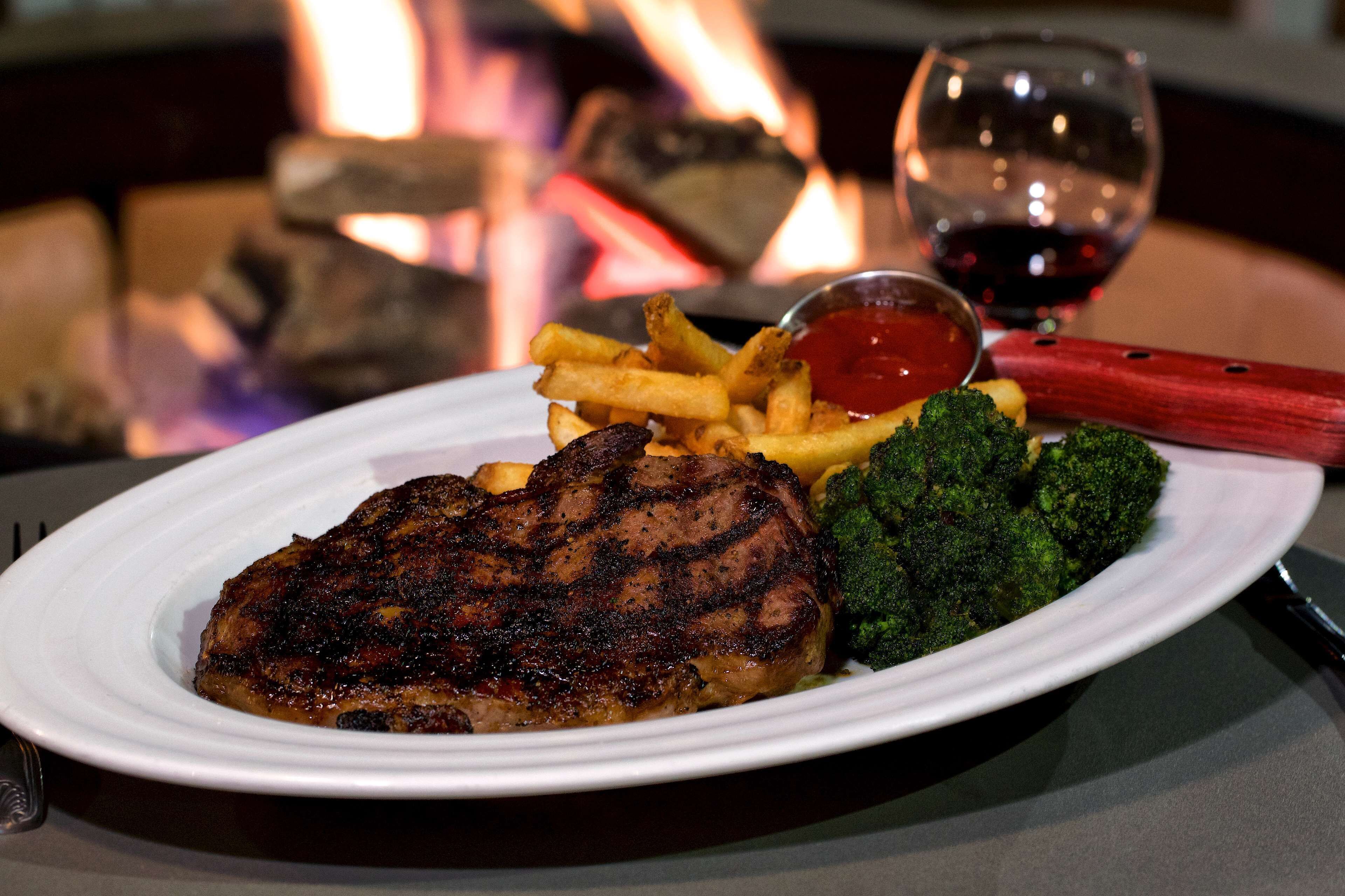 Un plato con carne a la parrilla, papas fritas, brócoli y una copa de vino tinto.