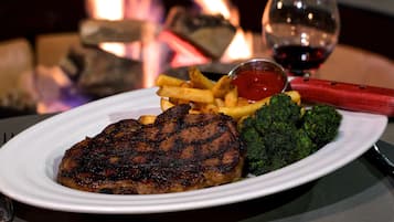 Un plato con carne a la parrilla, papas fritas, brócoli y una copa de vino tinto.