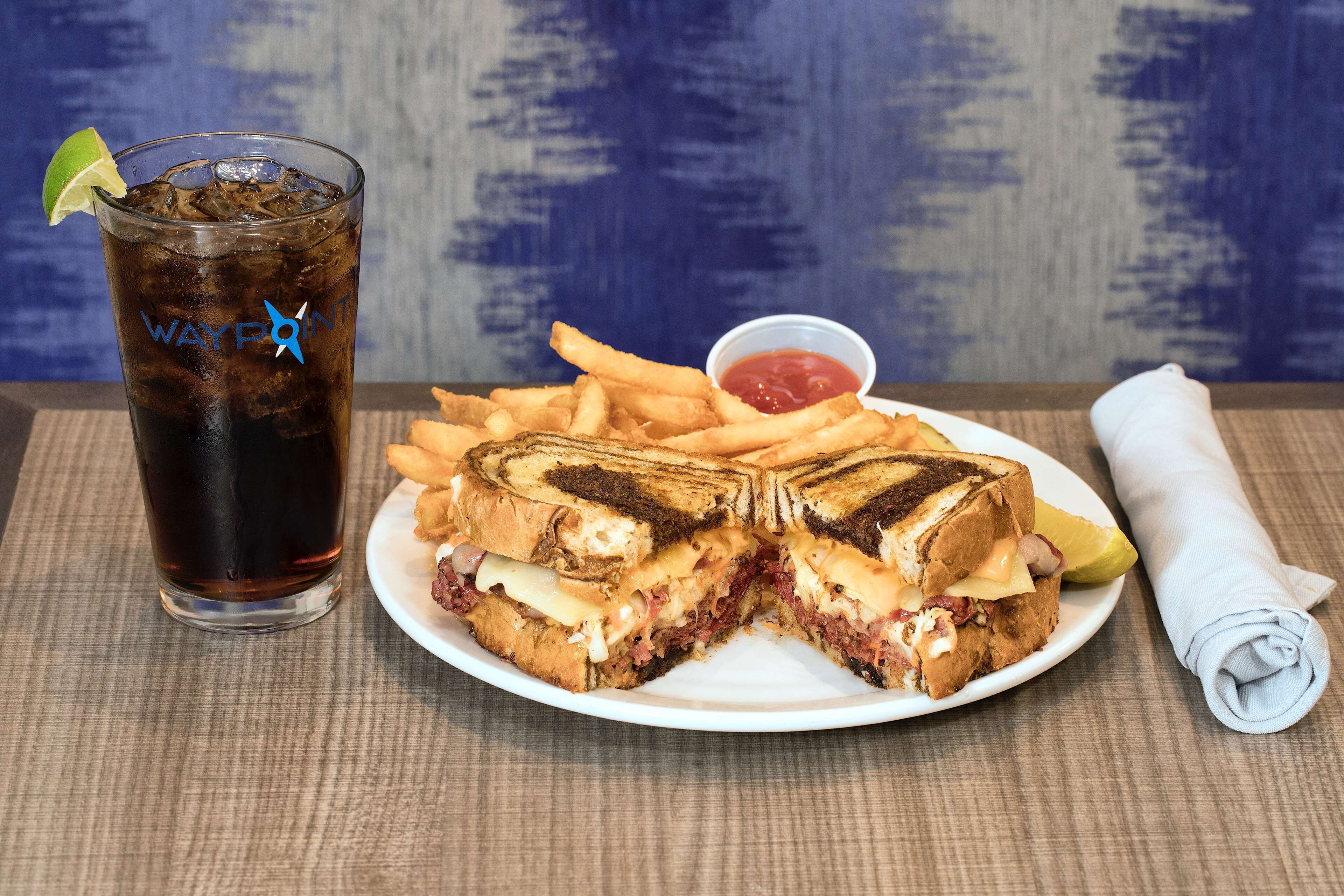 A plate with a grilled cheese sandwich, fries, and a drink with a lime wedge.
