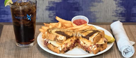 A plate with a grilled cheese sandwich, fries, and a drink with a lime wedge.