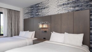 A hotel room with two beds, a stone-patterned wall, and a nightstand with a lamp. - Embassy Suites by Hilton Portland Maine (Portland)