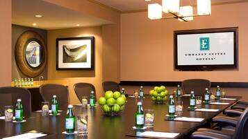 Un salón de conferencias con una larga mesa, sillas y una pantalla de proyector que muestra el logotipo de Embassy Suites Hotels.