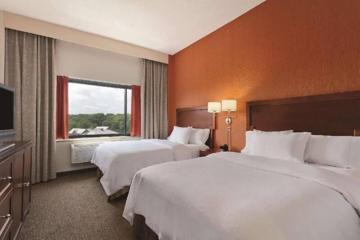 Une chambre d’hôtel avec deux lits, une télévision, une fenêtre avec des rideaux et une lampe.