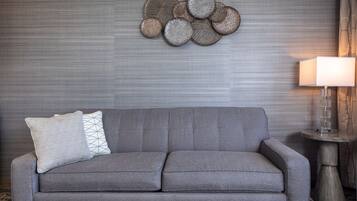 A grey sofa with two pillows, a wall-mounted decorative piece, and a table lamp.