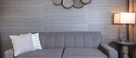 A grey sofa with two pillows, a wall-mounted decorative piece, and a table lamp.