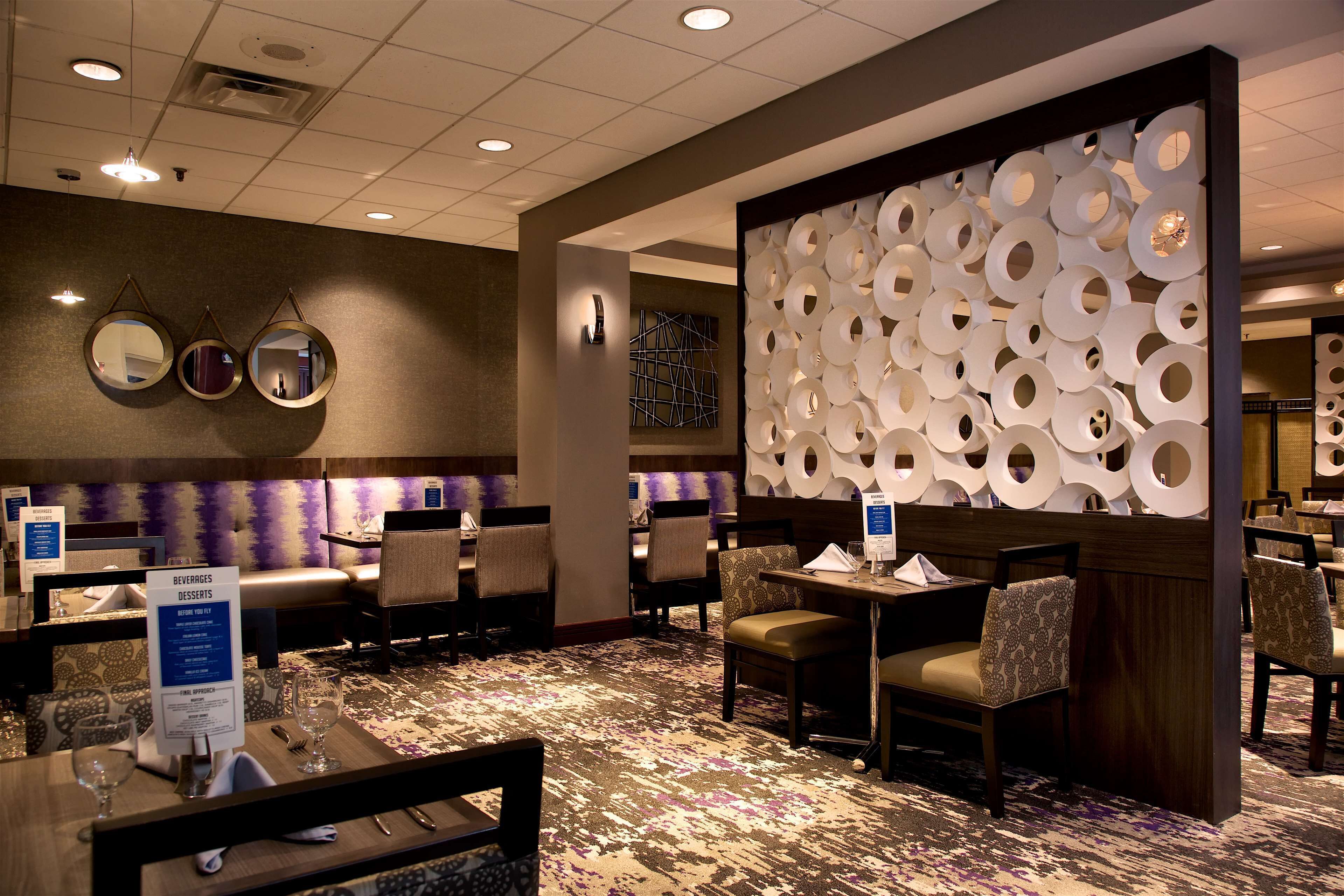 Comedor de hotel con mesas redondas, sillas y una pared decorativa con diseños circulares.
