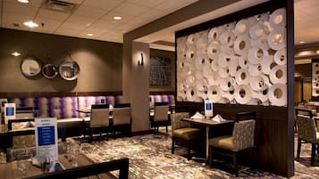 Comedor de hotel con mesas redondas, sillas y una pared decorativa con diseños circulares.