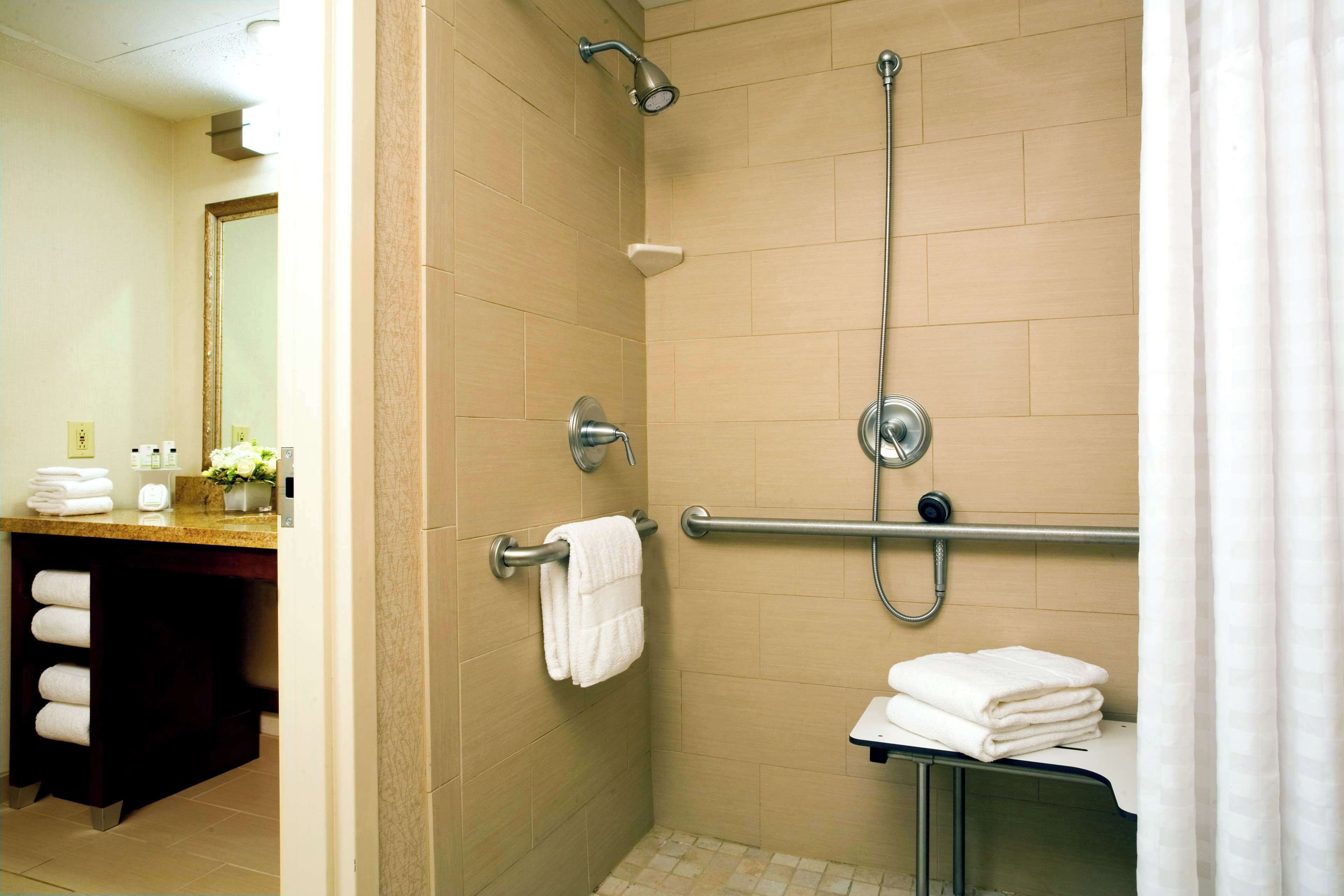 A shower area with a handrail, a towel rack, and a small sink with a mirror.