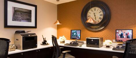 Een receptiebalie in een hotel met een lijst, een klok, twee monitoren, printers en bureaustoelen.