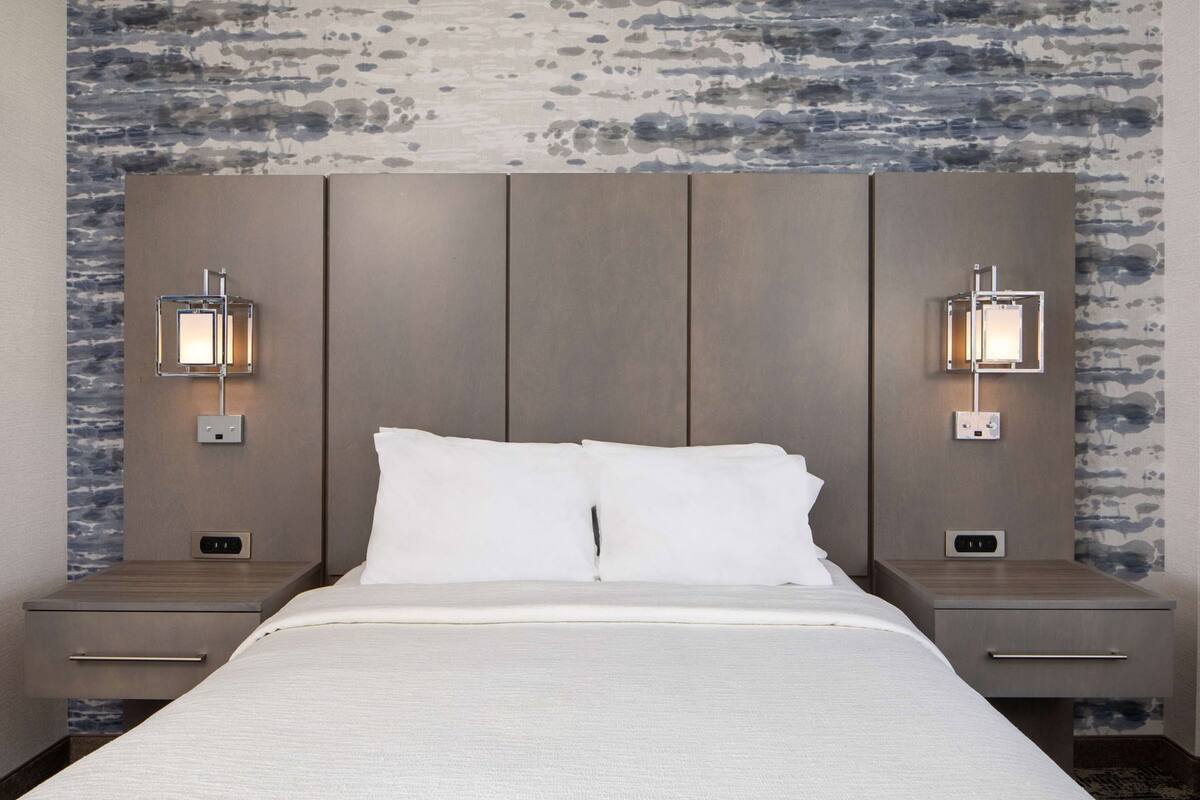 Une chambre d’hôtel avec un grand lit, deux tables de chevet et des lampes de lecture fixées au mur.