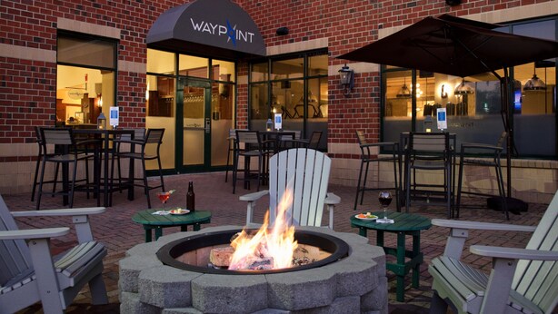 A brick building with a sign reading "WAYPOINT" and outdoor seating with tables, chairs, and a fire pit. - Embassy Suites by Hilton Portland Maine (Portland)