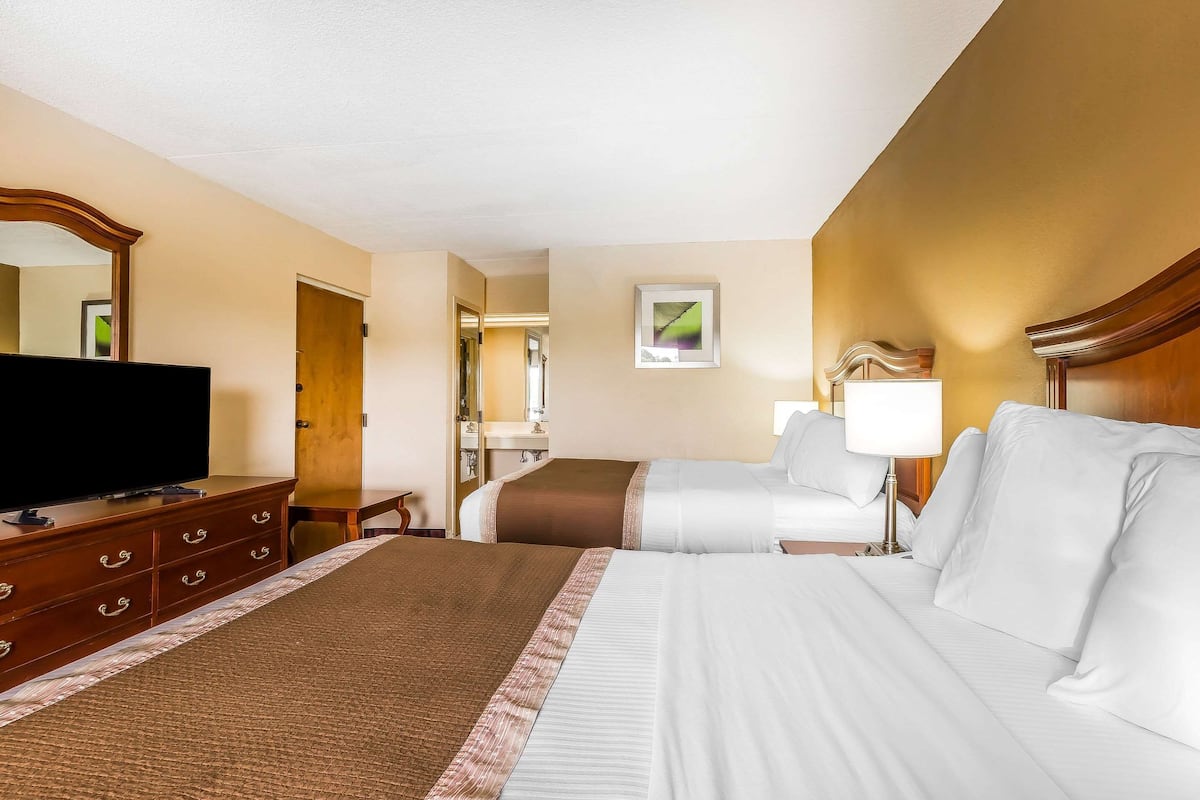 Una habitación de hotel con una cama grande, un televisor en un aparador de madera, un baño con espejo y un cuadro en la pared.