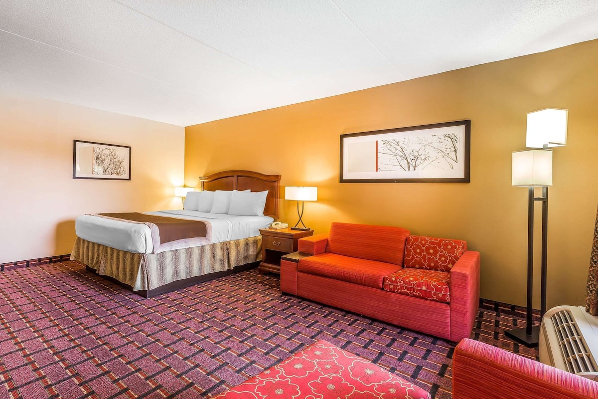 Una habitación de hotel con cama, sofá, mesita de noche, lámpara y lámpara de pie.
