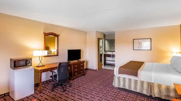 A hotel room with a bed, desk, chair, microwave, refrigerator, and a television.