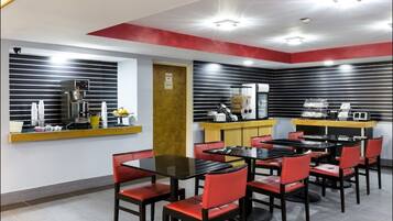 A modern cafe with black and red chairs, a coffee machine, and a counter with a cash register.