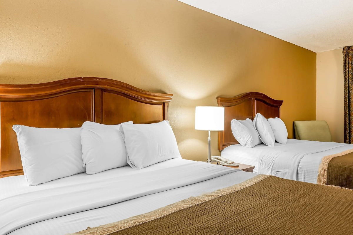 Habitación de hotel con dos camas, una mesita de noche con lámpara y una silla.