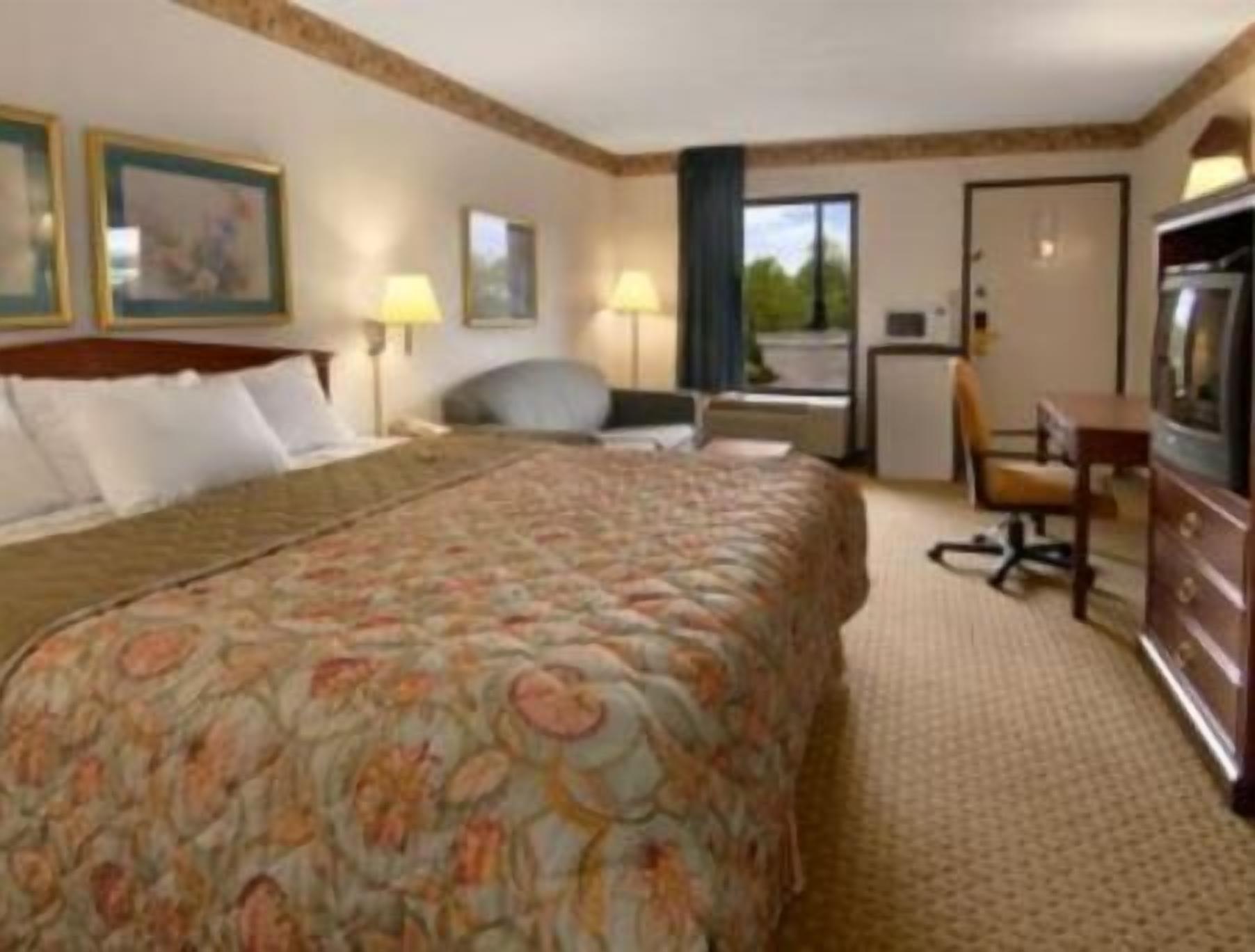 A hotel room with a bed, desk, chair, TV, and a window.