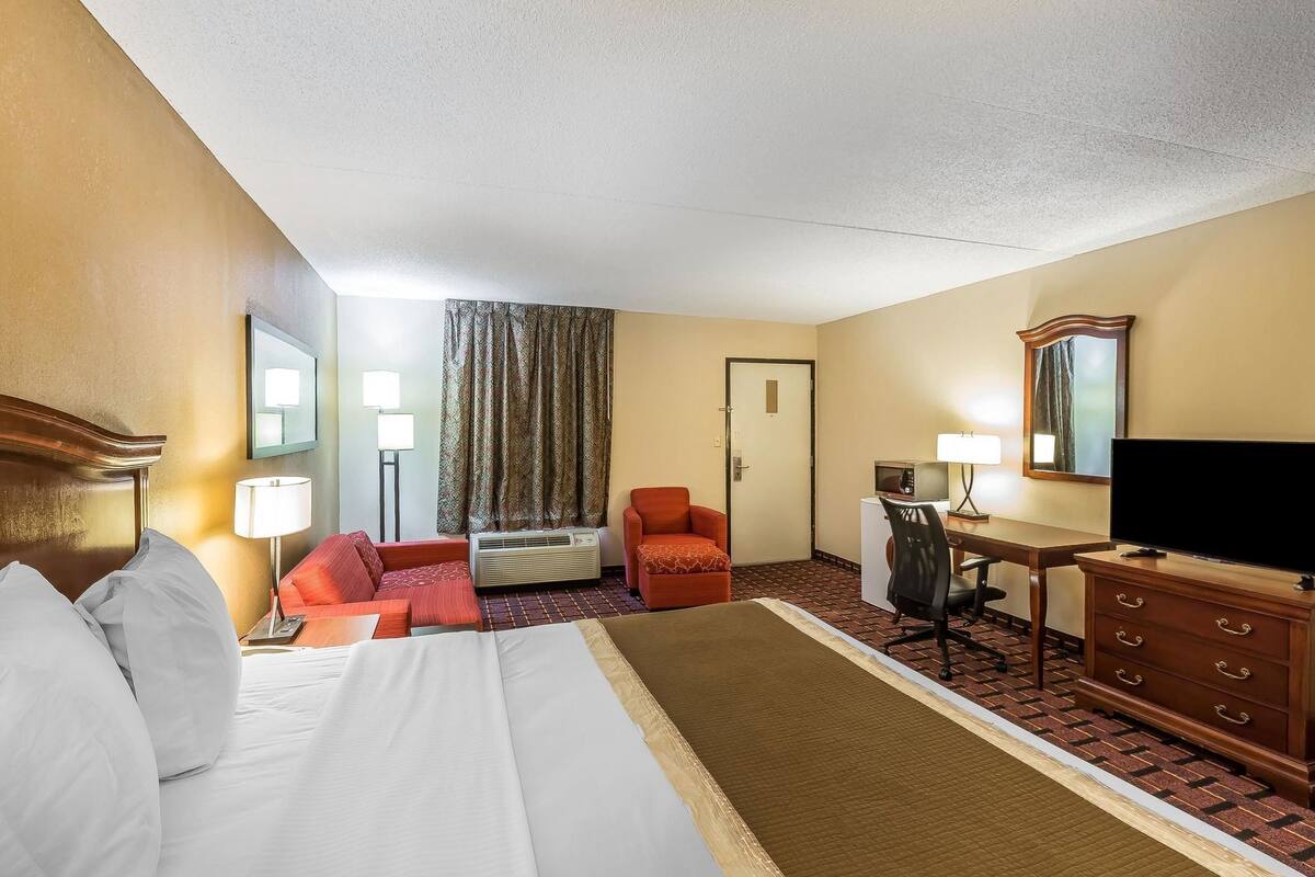 A hotel room with a bed, a desk, a chair, a television, and a window with curtains.