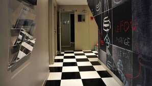 A hallway with a checkered floor, a door leading to a room, and a wall with chalk drawings. - ibis Styles Rouen Nord Barentin (Barentin)