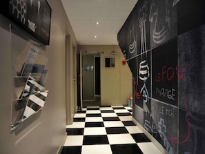 Un couloir avec un sol à carreaux, une porte donnant sur une pièce et un mur orné de dessins à la craie.