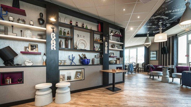 A bar area with shelves of bottles, glasses, and a foosball table. - ibis Styles Rouen Nord Barentin (Barentin)