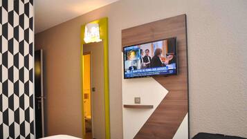 A hotel room with a bed, a television mounted on the wall, a mirror, and a suitcase.