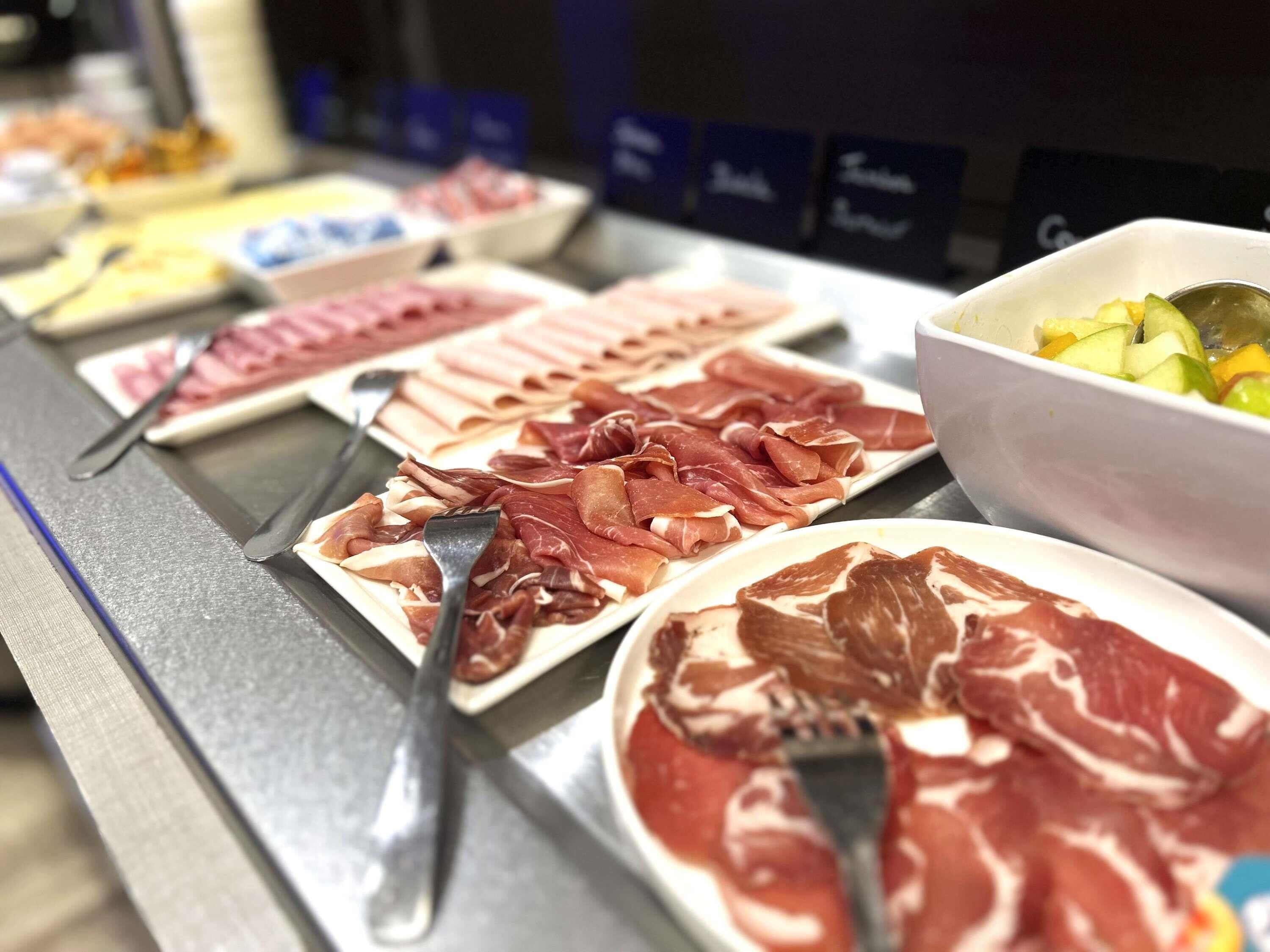 A buffet with various meats and a bowl of fruit salad.