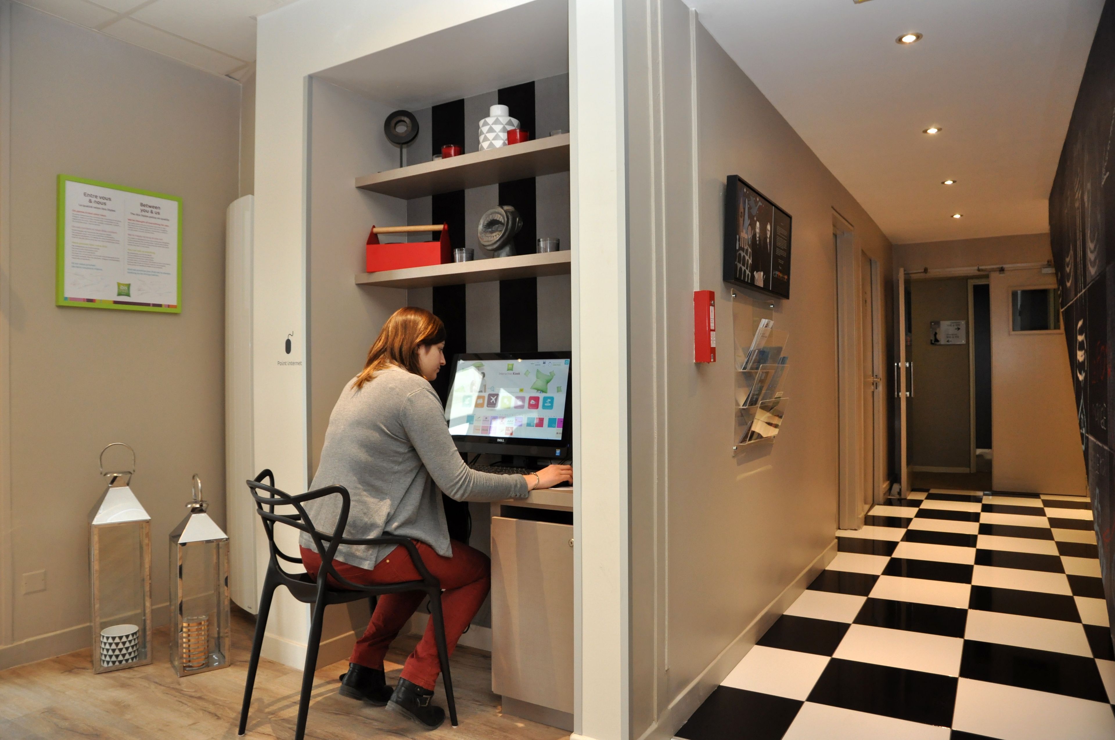 A woman working at a desk in a modern office space with a checkered floor and a whiteboard on the wall.