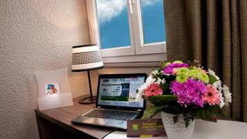 A laptop on a desk with a lamp, a bouquet of flowers, and a welcome sign.