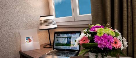 Una laptop sobre un escritorio con una lámpara, un ramo de flores y un cartel de bienvenida.