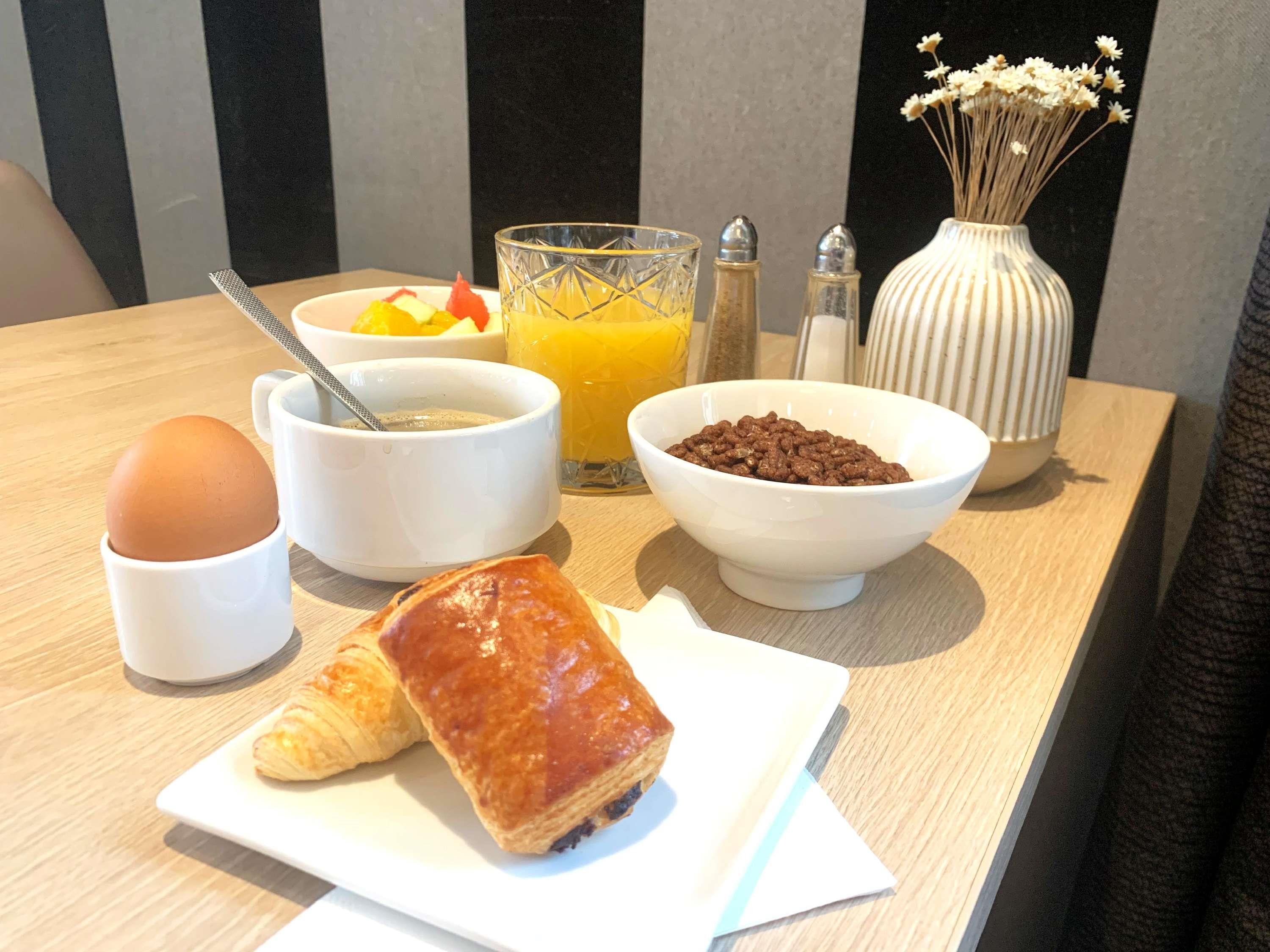 Een ontbijttafel met een croissant, een kom ontbijtgranen, een glas sinaasappelsap en een kop koffie.