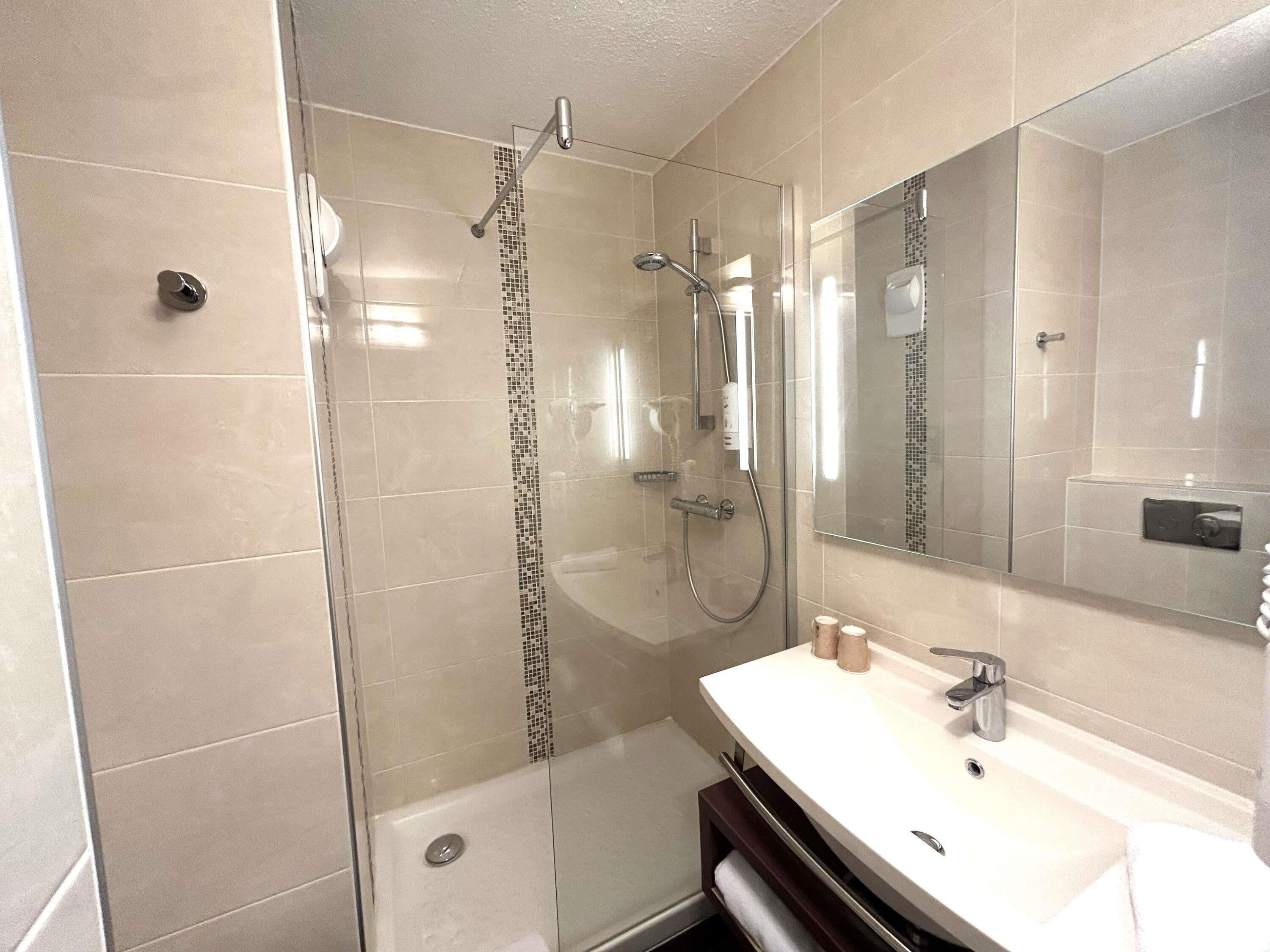 A modern bathroom with a glass-enclosed shower, a white sink, and a large mirror.