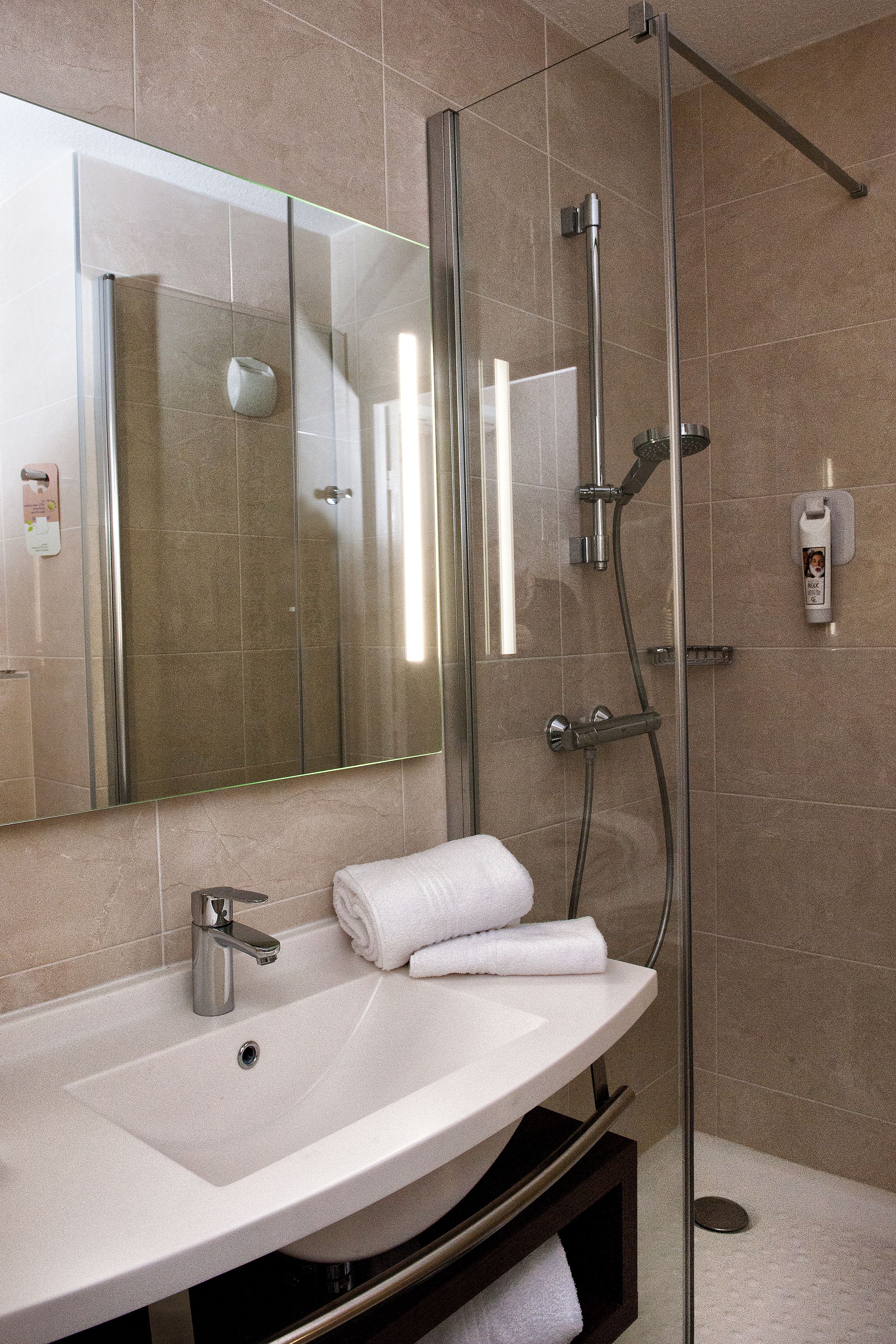 A modern bathroom with a glass-enclosed shower, a white sink, and a large mirror.
