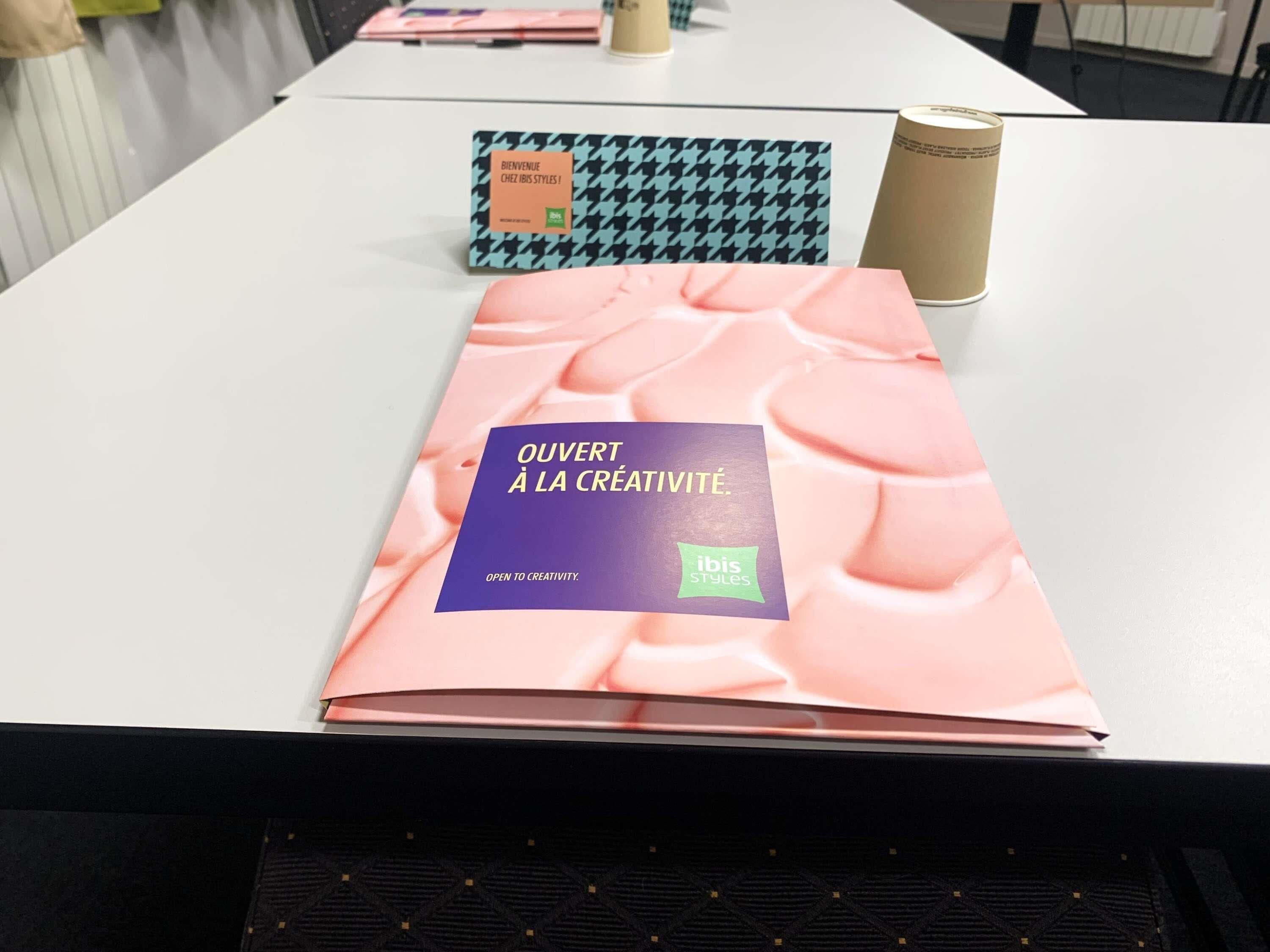 A table with a book titled 'OUVERT À LA CRÉATIVITÉ' and a houndstooth-patterned box with 'BIENVENUE' on it.